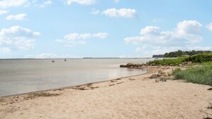 A sandy beach with calm water, scattered rocks, and a distant shoreline with vegetation. - 2 bedroom beach front home in Sjølund (Sjølund)