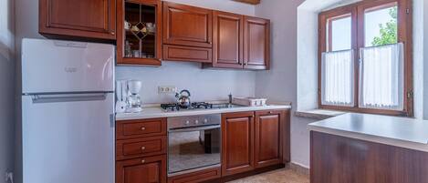 A kitchen with wooden cabinets, a white refrigerator, a stove, and a window with curtains.
