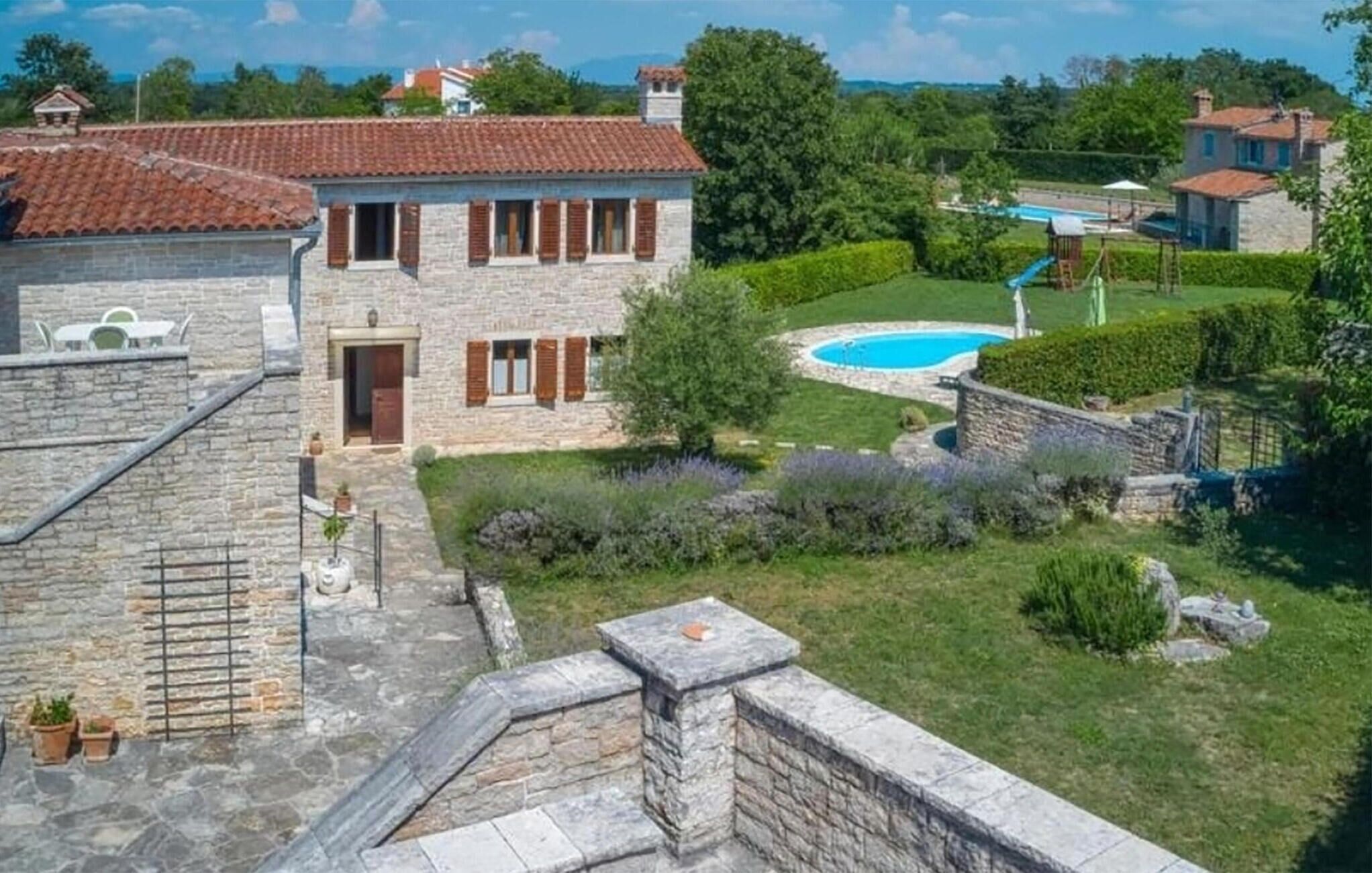 Una casa de piedra con techo de tejas, piscina y jardín bien cuidado.