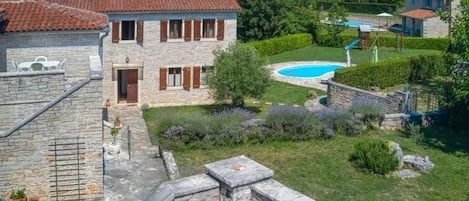 Una casa de piedra con techo de tejas, piscina y jardín bien cuidado.