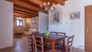 Un espace repas comprenant une table et des chaises en bois, un lustre, un mur en pierre et un canapé en cuir.