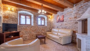 Un salon chaleureux avec des murs en pierre, un plafond en bois, un canapé en cuir, un téléviseur posé sur un meuble en bois et une cheminée.
