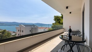 A balcony with a table and chairs, a bottle of wine, and a view of a bridge over water. - Luxurious home in Komarna (Komarna)
