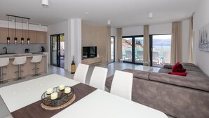 A modern living room with a sofa, a dining table with candles, and a TV. - Luxurious home in Komarna (Komarna)
