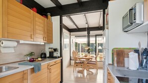 A modern kitchen with wooden cabinets, a dining area with a table and chairs, and a large window providing natural light. - Gorgeous home in Gørlev with WiFi (Gørlev)