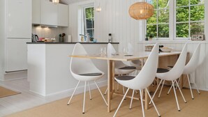 A modern kitchen with white cabinetry, a wooden island, and a dining area with white chairs and a wooden table. - Amazing home in Gilleleje with WiFi (Gilleleje)