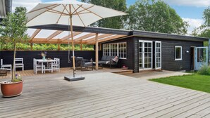 A modern outdoor patio with a wooden deck, a covered seating area with a table and chairs, and a large umbrella. - Amazing home in Gilleleje with WiFi (Gilleleje)