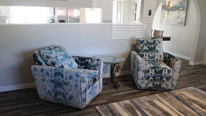 Un salon avec deux fauteuils à motifs bleus, une table basse en verre et un tapis rayé.