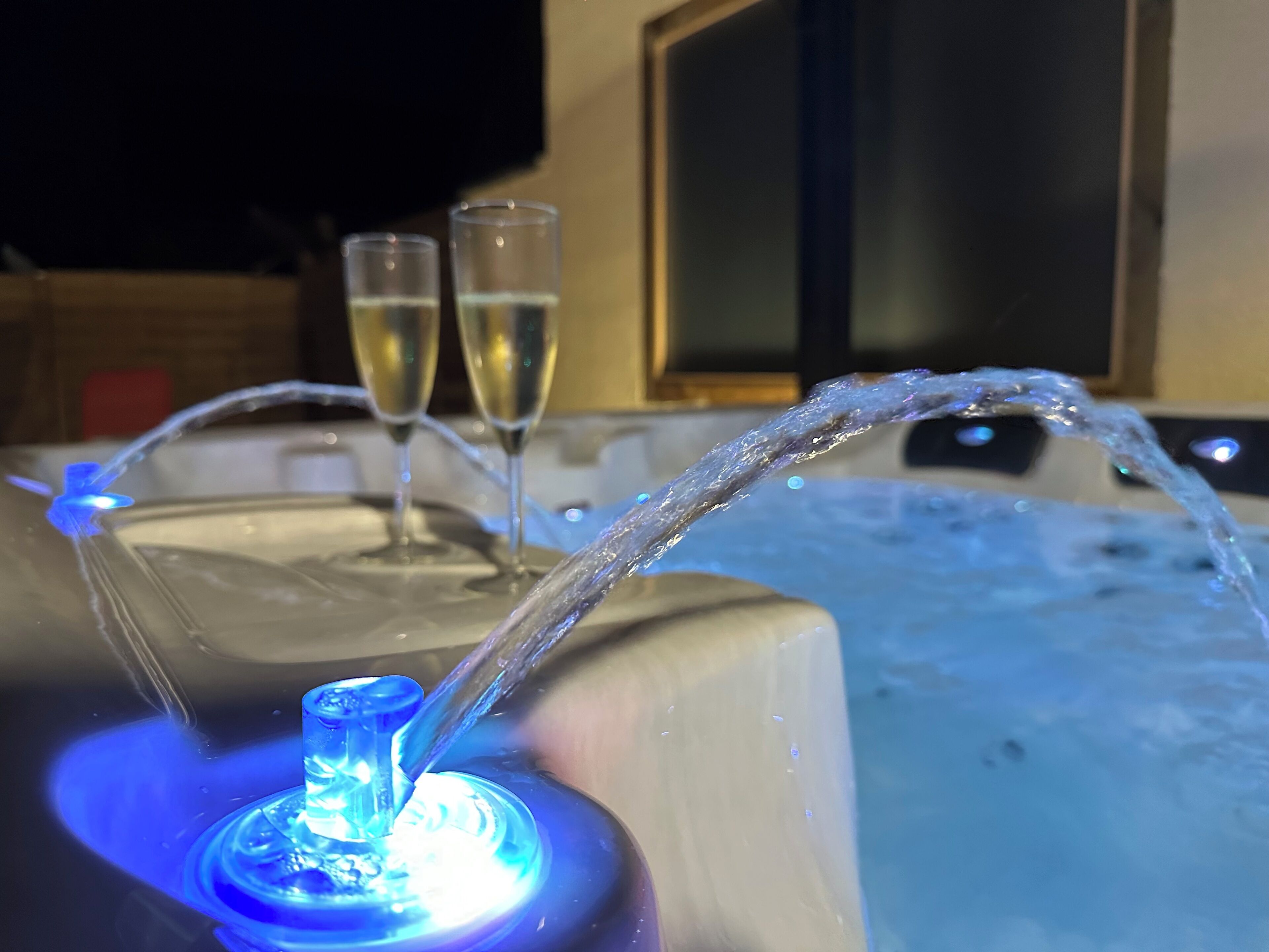 A hot tub with a water fountain feature and two glasses of champagne.