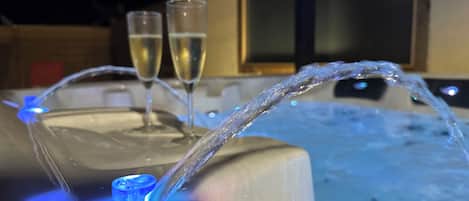 A hot tub with a water fountain feature and two glasses of champagne.