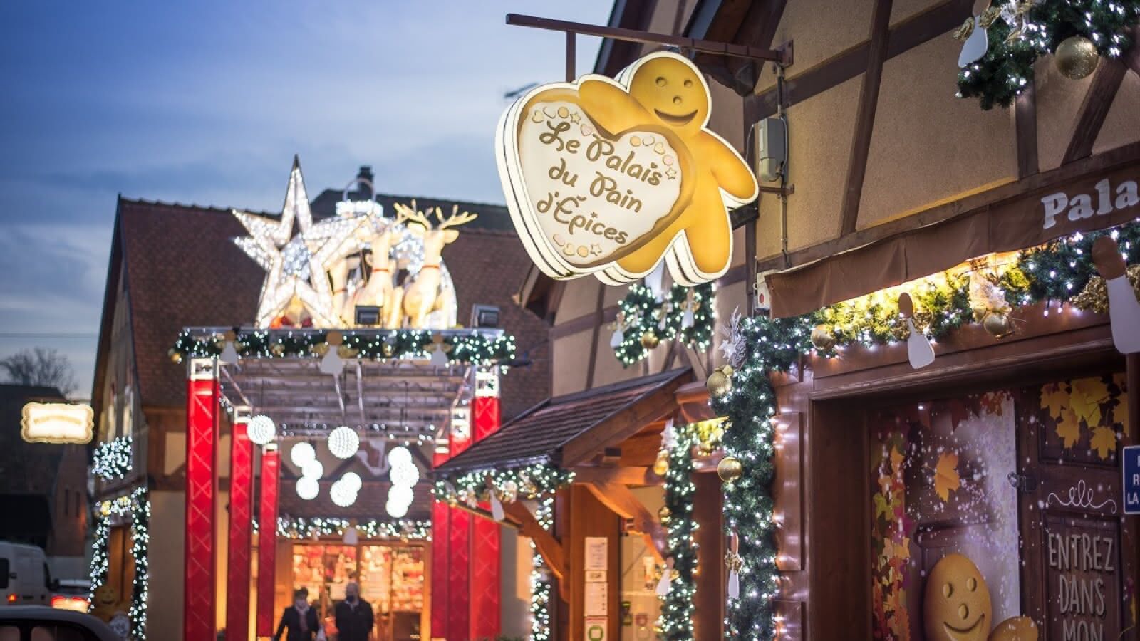 A building facade with a sign reading "Le Palais du Pain d'Epices" and a gingerbread man decoration.