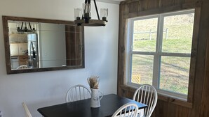 A dining area with a black table, white chairs, a large mirror, and a chandelier. - Romantic cottage, pet friendly, stunning views of Smoky mtns. & Pigeon River.  (Clyde)