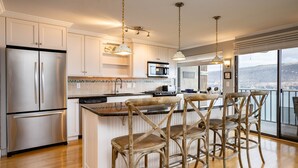 A modern kitchen with stainless steel appliances, a large island with bar stools, and a view of the city through large windows.