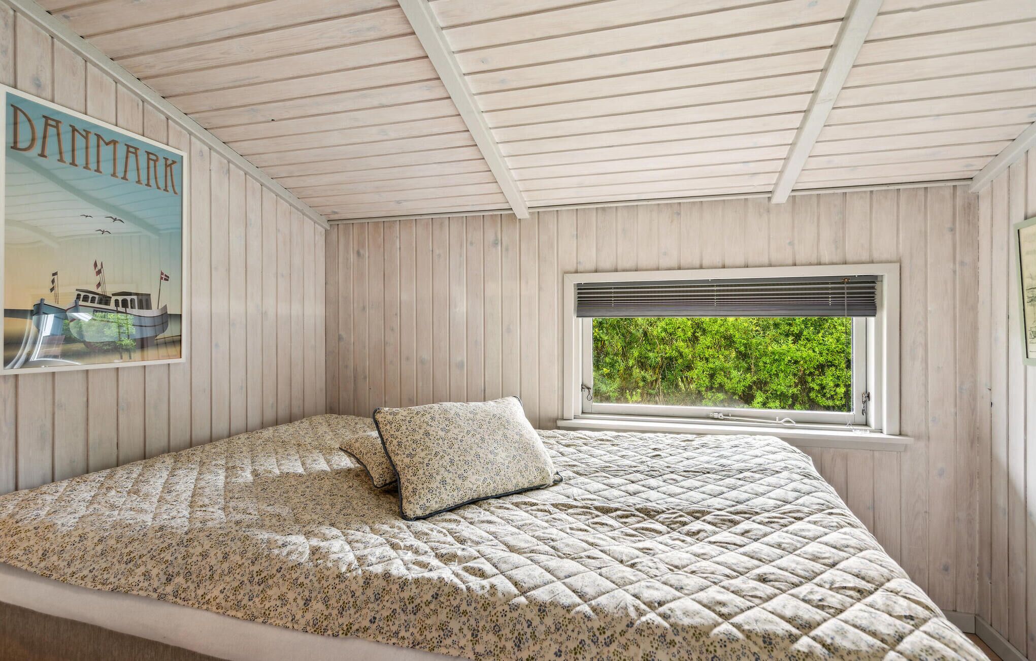 A bedroom with a bed, a window with a view of greenery, and a poster on the wall.