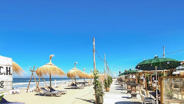 Ein Strandbereich mit Liegestühlen, Reetdachschirmen und Gartenmöbeln.