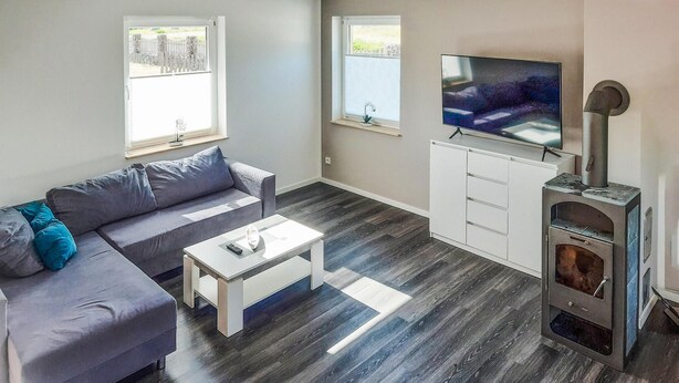 Un salon moderne avec un canapé gris, une table basse blanche, un téléviseur et un poêle à bois.