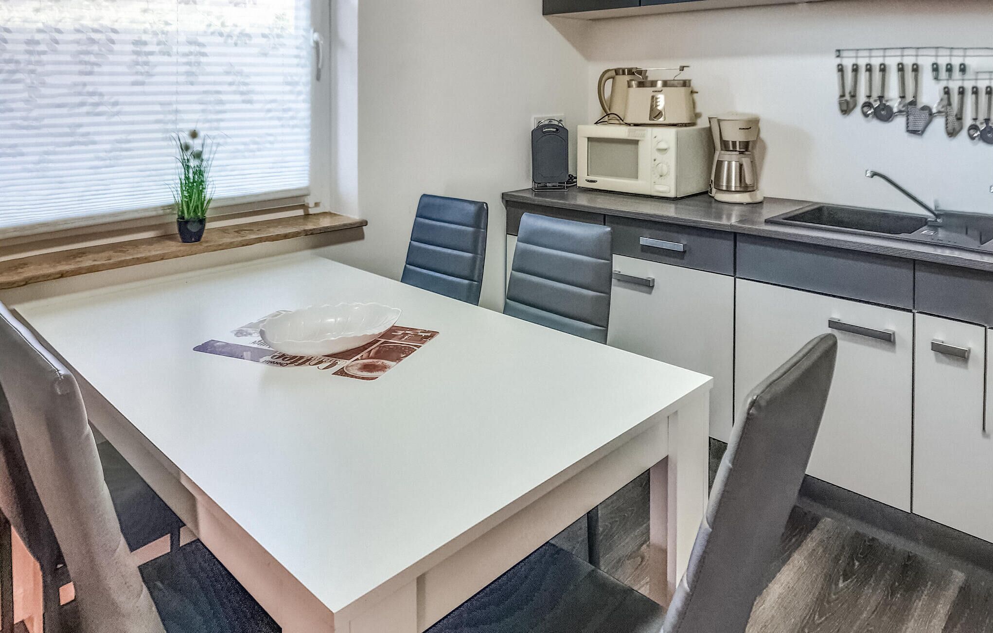 Una cocina moderna con una mesa blanca, sillas azules, una cafetera y un microondas.