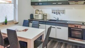 Une cuisine compacte avec un coin repas, équipée d’un four à micro-ondes, d’une machine à café et de divers ustensiles fixés au mur.