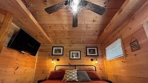 Ein gemütliches Schlafzimmer in einer Holzhütte mit Bett, Deckenventilator, Wand-Fernseher und gerahmten Bildern.