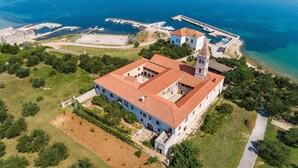 An aerial view of a coastal building with a red-tiled roof, adjacent to a marina with boats. - Beach front home in Pasman (Pasman)
