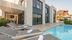 A modern outdoor pool area with lounge chairs and a glass-enclosed dining area. - Beach front home in Pasman (Pasman)