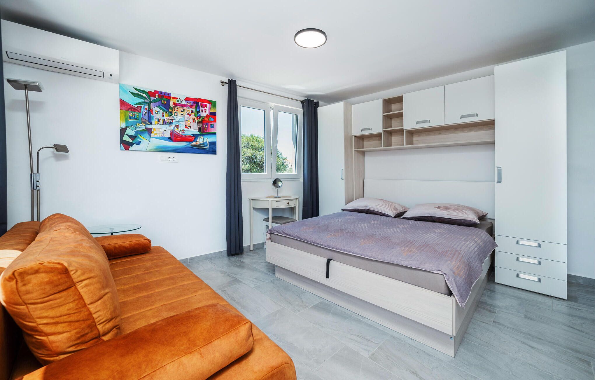 A modern bedroom with a bed, a sofa, a desk, and a painting on the wall.