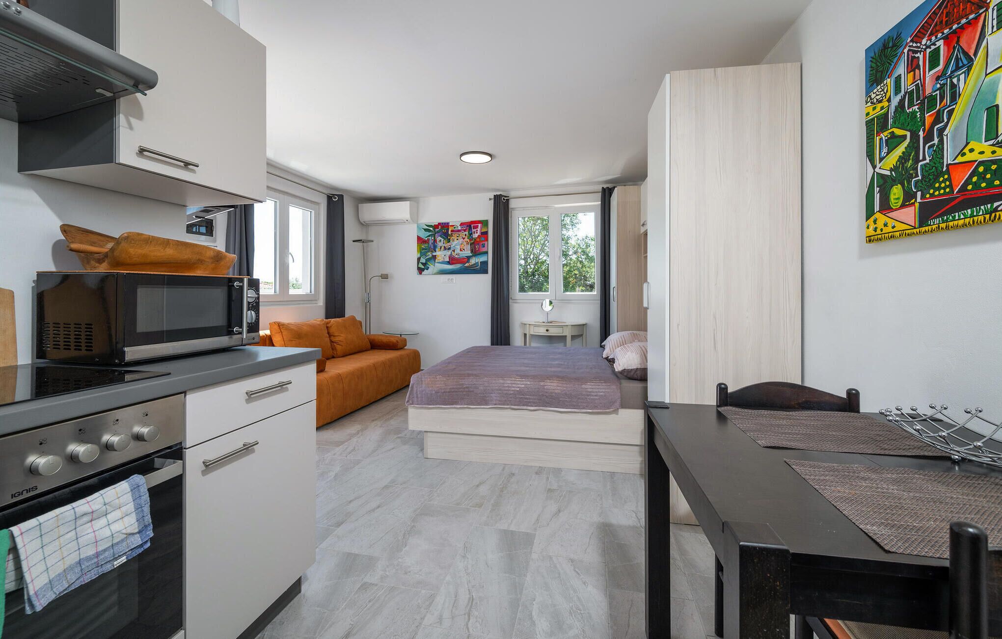 A compact hotel room with a kitchenette, a bed, a dining table, and a large window.
