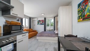 Habitación de hotel compacta con kitchenette, una cama, una mesa de comedor y un ventanal grande.