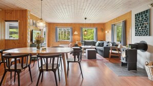 L’intérieur chaleureux d’un chalet avec un plafond en bois, un coin repas comprenant une table ronde et des chaises, un ensemble de canapés et une cheminée.