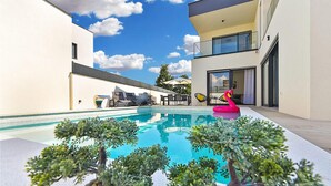 Uma área moderna de piscina ao ar livre, com uma piscina azul cristalina, rodeada por vasos de plantas e um boi flamingo flutuante.