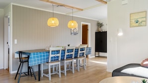 Un comedor con mantel a cuadros azules, sillas blancas, dos lámparas colgantes de mimbre y un aparador negro al fondo.