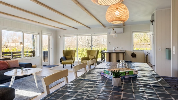 Un luminoso espacio de sala con plan abierto, que incluye una mesa de comedor, sillas y un sofá. Amplias ventanas ofrecen luz natural y vistas al exterior.