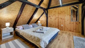 A bedroom with a sloped ceiling, wooden walls, a bed with patterned bedding, bedside tables with lamps, and a mirror on the wall. - Gorgeous home in Duga Resa with WiFi (Duga Resa)