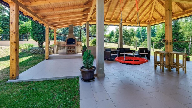 A covered outdoor patio with a wood-beamed structure, a stone fireplace, outdoor furniture, and a hanging swing. - Gorgeous home in Duga Resa with WiFi (Duga Resa)