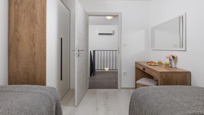 Une chambre d’hôtel avec deux lits, une armoire en bois, un petit bureau en bois avec un miroir, et une salle de bain visible à travers une porte ouverte.
