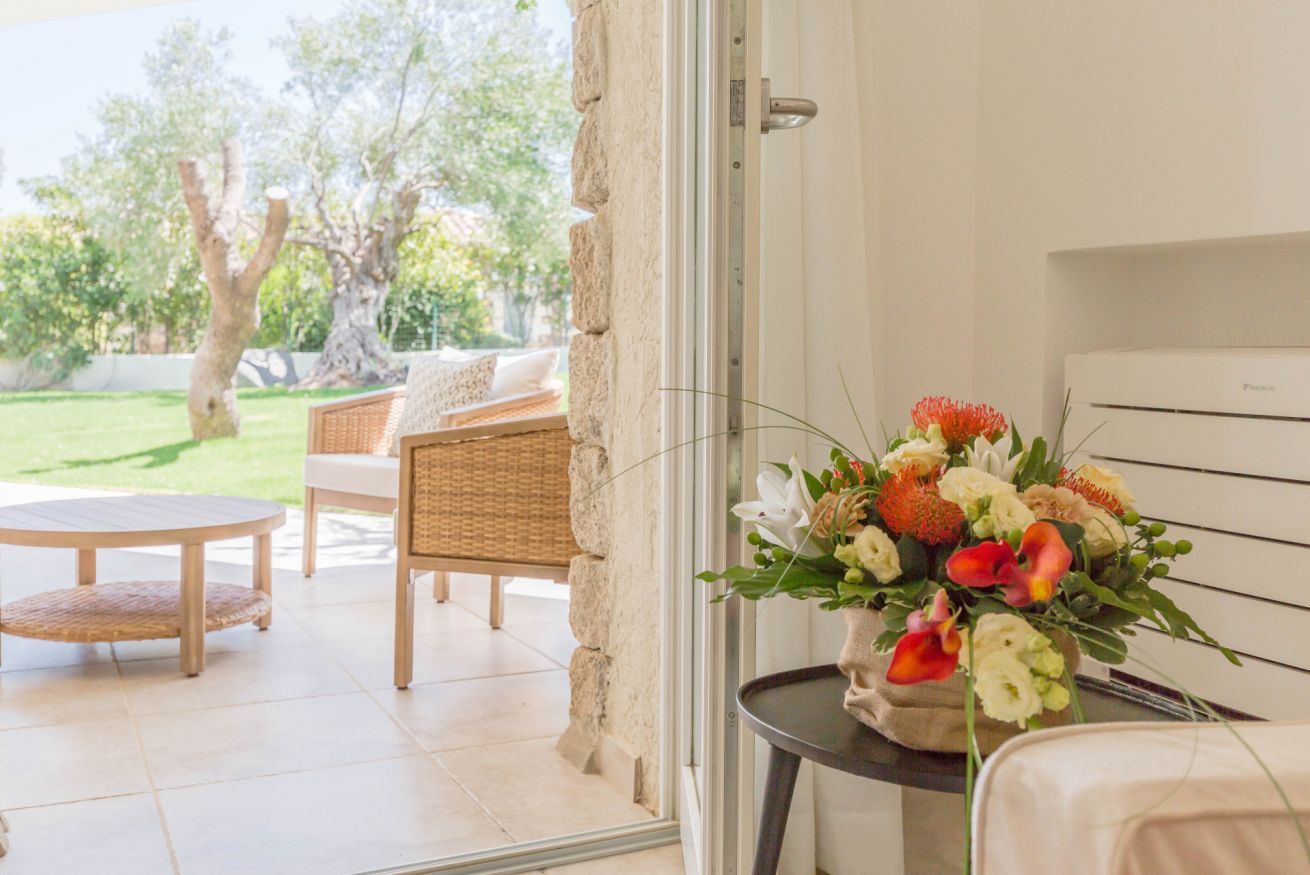A room with a wicker sofa, a round wooden table, and a potted plant with flowers.