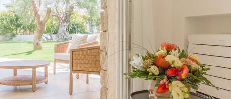 A room with a wicker sofa, a round wooden table, and a potted plant with flowers.