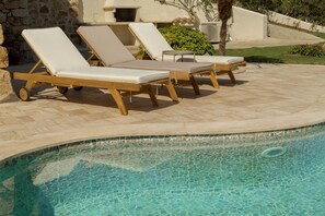 Zona junto a la piscina con sillones de descanso y una pared de piedra.