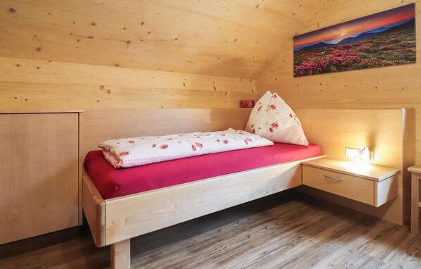 Una habitación de cabaña de madera con una cama individual, una mesita de noche, un armario pequeño y un cuadro en la pared.