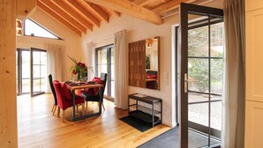 Un comedor con una mesa de madera, sillas rojas y un florero. Hay un espejo en la pared y una puerta que da al exterior.