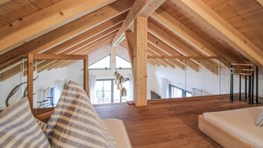 Un dormitorio en el ático con vigas de madera, techo inclinado, una cama y una escalera que lleva al piso principal.