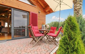 Una terrazza esterna con tavolo in legno e sedie rosse, un pilastro in pietra e vista sul verde circostante.