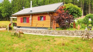 Una casa de madera con techo de tejas, contraventanas rojas y un muro de piedra frontal.