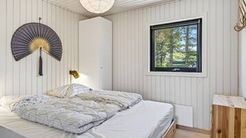Ett sovrum med en säng, ett fönster med utsikt över träd, en väggmonterad fläkt och ett nattduksbord.