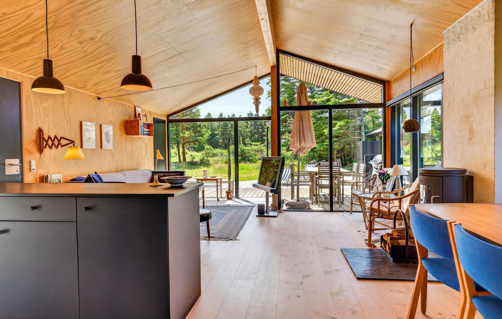 Une cuisine moderne dotée d’un grand îlot central, d’un plafond en bois et de grandes fenêtres offrant une vue sur l’extérieur.