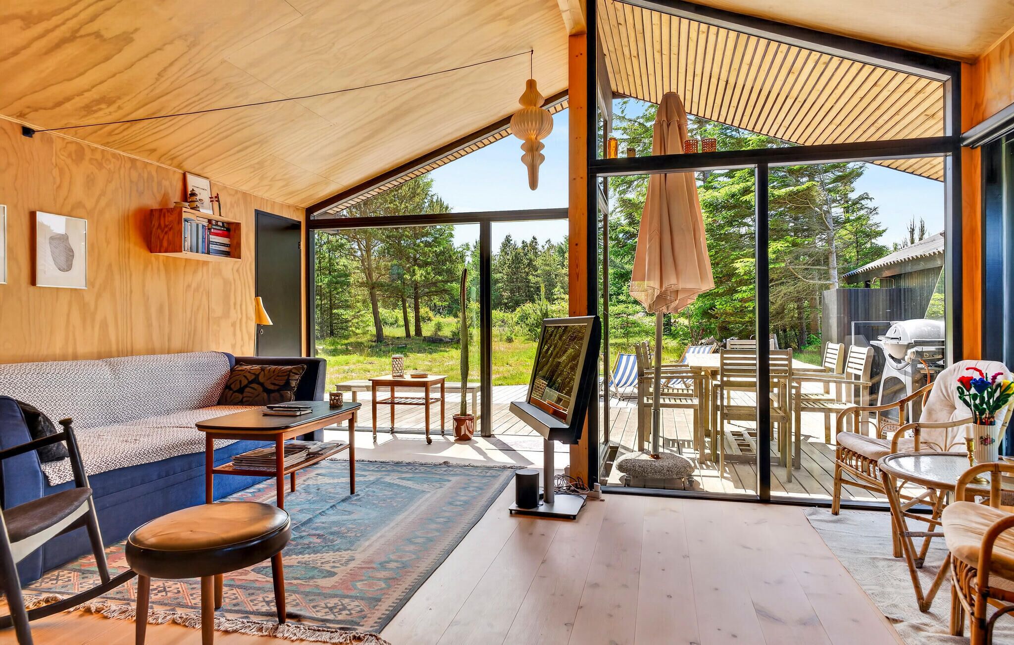 Un interior moderno con techo de madera, un sofá, un comedor con sillas y una mesa, y un gran ventanal que da a un espacio exterior.