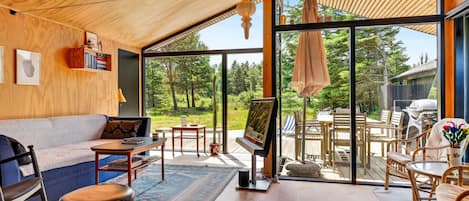 A modern interior with a wooden ceiling, a sofa, a dining area with chairs and a table, and a large glass door leading to an outdoor space.