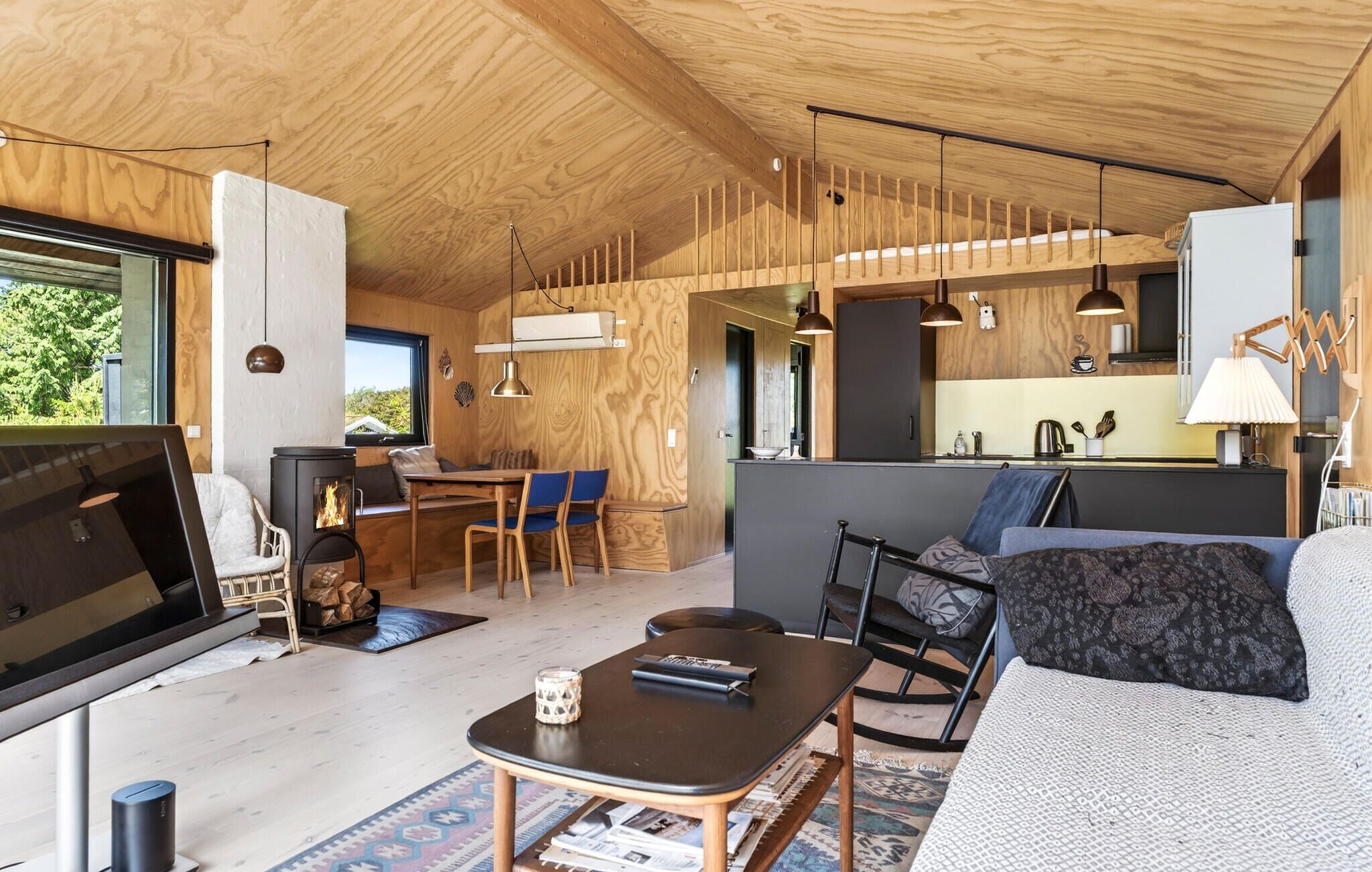 A modern interior with a wooden ceiling, a dining area, a kitchen, and a living space with a sofa and a TV.
