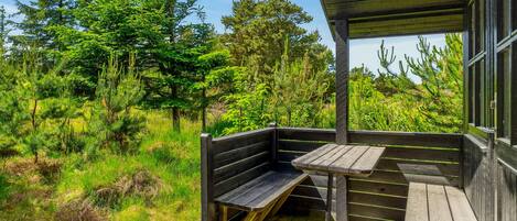 Eine Holzterrasse mit Bänken und einem Tisch, umgeben von dichtem Grün und Bäumen.