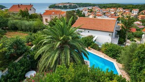 A residential area with a swimming pool surrounded by lush greenery and a view of the sea.